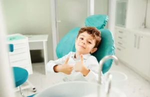 Niño sonriente en un sillón dental durante una revisión por apiñamiento dental, haciendo el gesto de pulgares arriba.